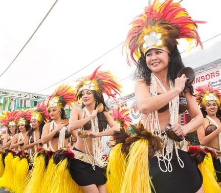 Group of Manea Florida Polynesian dancers smiling and performing in traditional feathered headdresses and yellow grass skirts at a Florida event